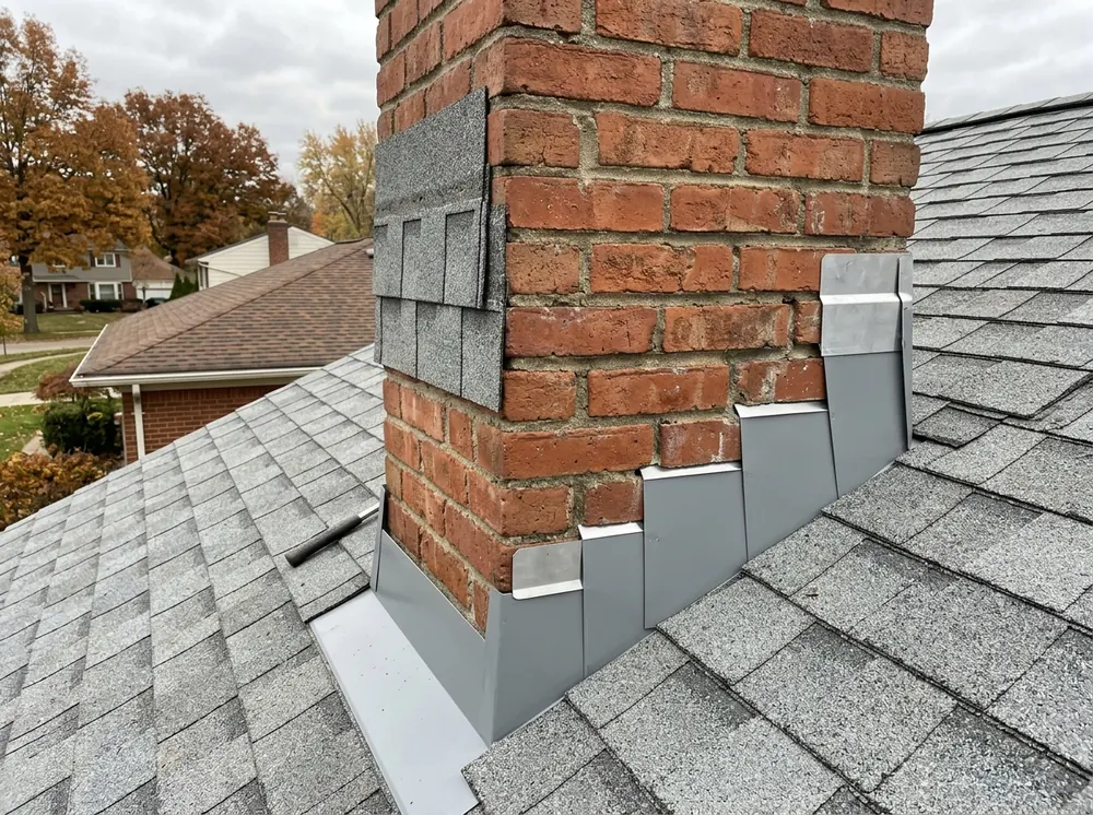 Close view of bent aluminum step flashing pieces interleaved with gray asphalt shingle courses along the side of a red brick chimney