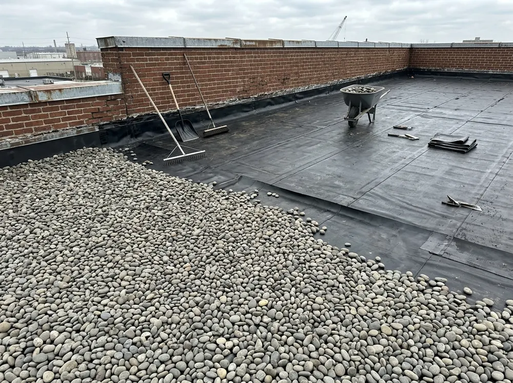 Black EPDM membrane on a flat roof partly covered with rounded river-stone ballast near a parapet wall
