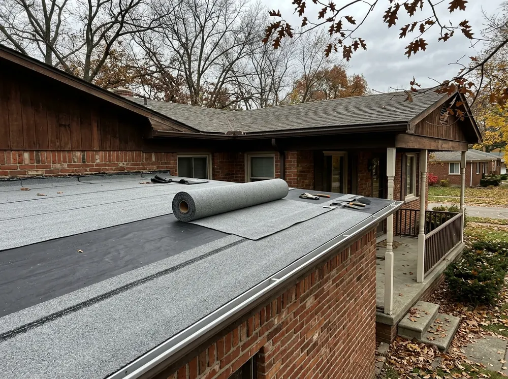 Roll of granule-surfaced modified bitumen cap sheet being unrolled and heat-sealed on a low-slope porch roof